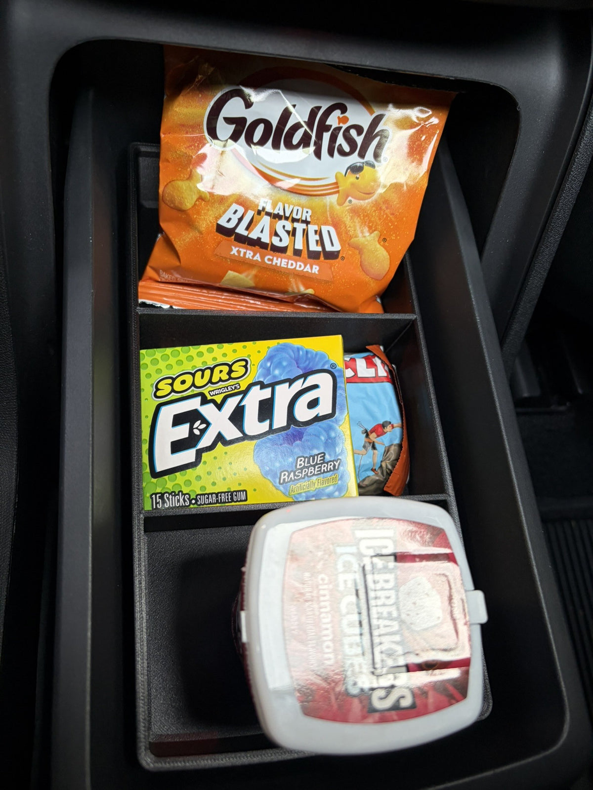 Slide-Out Drawer Tray in a Rivian R2 drawer holding crackers, gum, an energy bar and a mint container