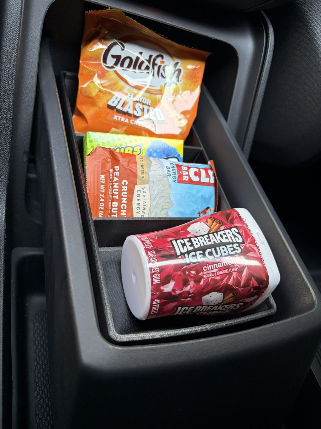 Slide-Out Drawer Tray in a partly open Rivian R2 console drawer holding crackers, an energy bar and a mint container